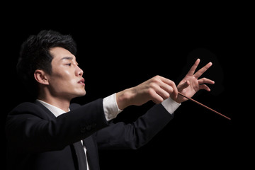 Young conductor with baton raised, black background - obrazy, fototapety, plakaty