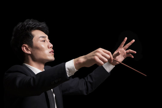 Young conductor with baton raised, black background