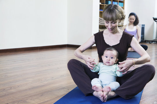 Mother And Baby Sitting Cross-legged And Doing Yoga In A Yoga Class