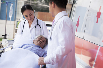 Two doctors wheeling in a elderly patient on a stretcher in front of an ambulance © xixinxing
