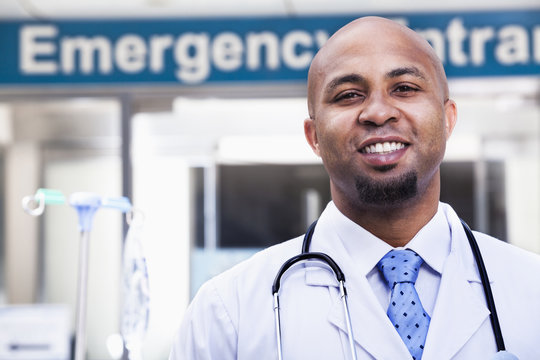 Portrait of smiling doctor outside of the hospital, emergency room sign in the background