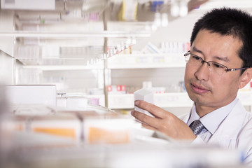 Naklejka na ściany i meble Pharmacist taking down and examining prescription medication in a pharmacy