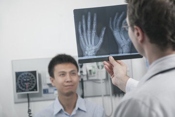 Fototapeta premium Doctor holding up and looking at x-ray of patients hand bones, patient in the background