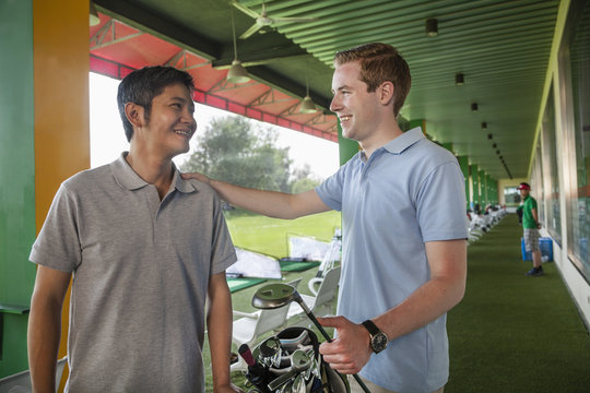 Two male friends talking and smiling while playing golf