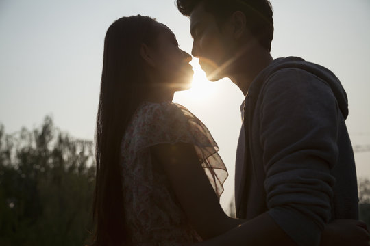 Silhouette of young couple very close to each other, sunbeam and lens flare 