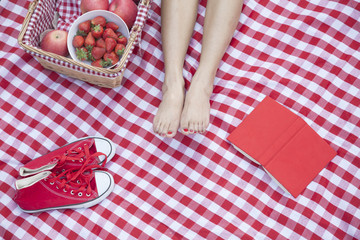 Obraz premium Young woman's feet on a checkered blanket with a picnic basket, shoes, and a book 