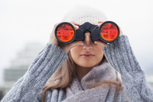 Cute woman with winter clothes on looking through binoculars