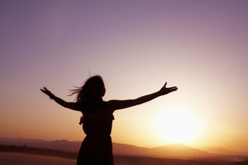 Serene young woman with arms outstretched doing yoga in the desert in China, Silhouette