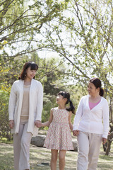 Multi-generational family, grandmother, mother, and daughter holding hands and going for a walk in the park in springtime