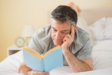 Fototapeta premium Concentrated man reading a book on his bed