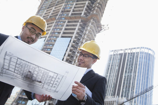 Architects looking at blueprint on construction site, Beijing
