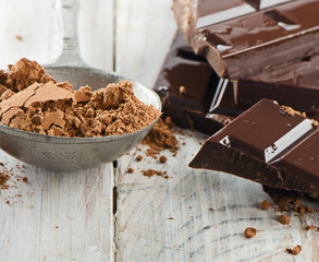 Cocoa powder and broken chocolate bar and on a wooden table
