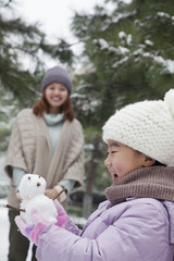 Girl Holding a snowman in a park with mother