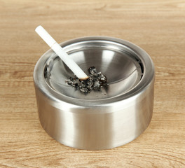 Metal ashtray and cigarette on wooden table