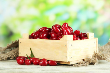 Fresh cornel berries in wooden crate on table, outdoors