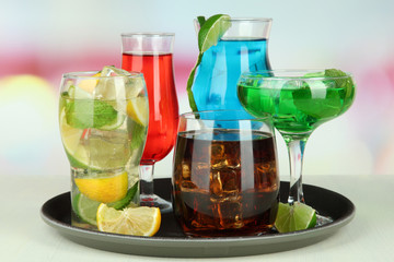 Many glasses of cocktails on tray on table, on bright