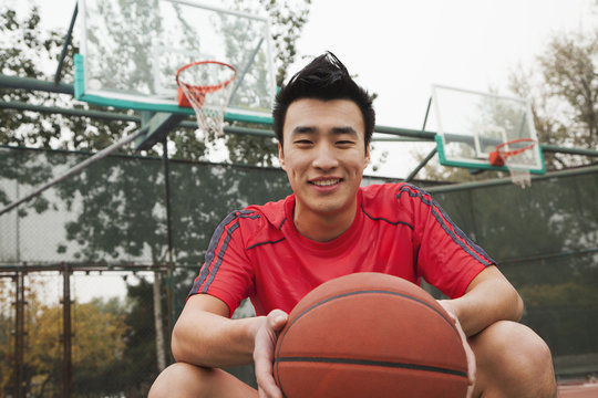 Young man sitting with a basketball on the basketball court, portrait  