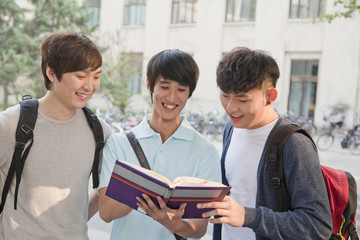 Three students discussing and looking at the book 