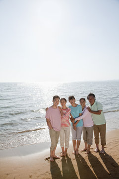 Multi generational family portrait, arms around each other by the beach
