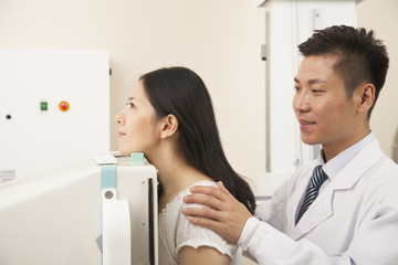 Male Doctor Examining Female Patient's Mid Section With X-ray Machine
