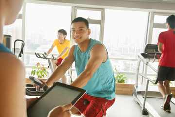 Obraz premium Young man on stationary bike exercising with his personal trainer