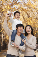 Boy sitting on his fathers shoulders in a park with family in Autumn