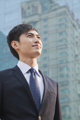 Young Businessman Looking Up, Glass Building, Portrait