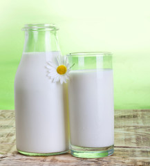 Milk bottle and glass on wooden desk with chamomile.