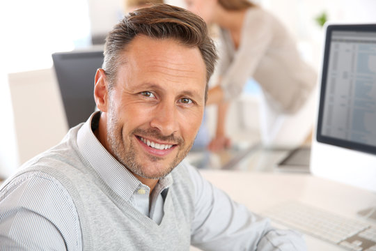 Cheerful man sitting in office and working on desktop