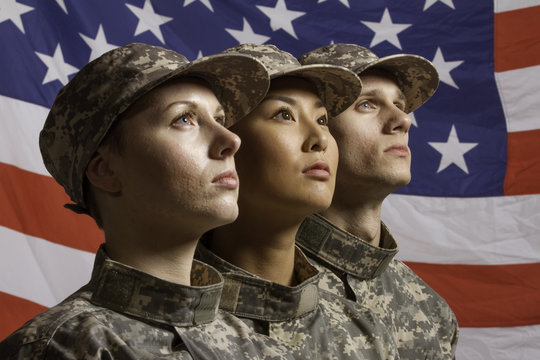 Three young military personnel in front of flag, horizontal