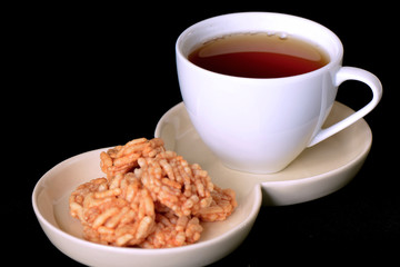 Afternoon tea and crispy rice snack on black background.