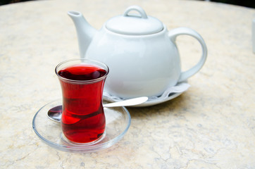 Traditional turkish glass of fruit tea and white ceramic teapot