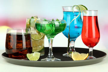 Many glasses of cocktails on tray on table, on bright