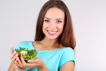 Beautiful girl with fresh salad on grey background