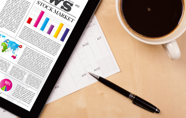 Tablet pc shows news on screen with a cup of coffee on a desk