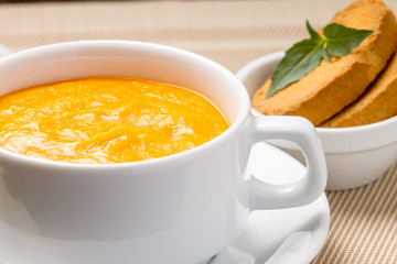 Pumpkin soup in white bowl with fresh basil