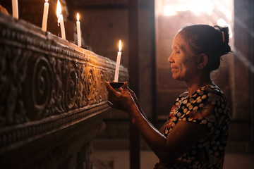 Asian woman praying with candle light - obrazy, fototapety, plakaty