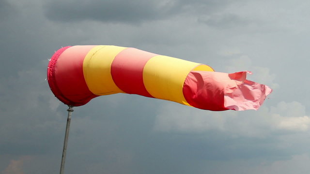 Wind sock with rainy stormy clouds background. Red and yellow