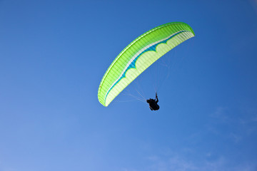 Green paraglider flying in blue sky.