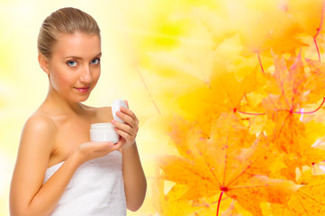 Young girl with body cream jar on autumnal background