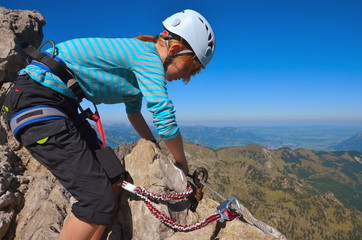 Kind mit Sicherung, Klettergurt und Helm am Klettersteig