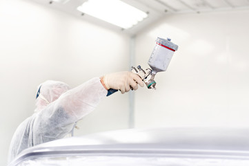 Worker using a paint spray gun for painting a car in garage