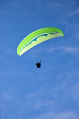 Green paraglider flying in blue sky.