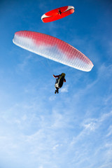 Two paragliders flying in blue sky.