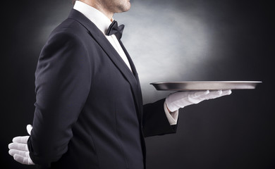 Waiter holding empty silver tray over black background