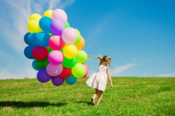 Little girl holding colorful balloons. Child playing on a green
