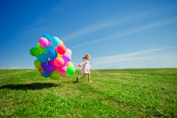 Little girl holding colorful balloons. Child playing on a green
