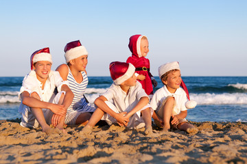 Children in santa claus hat are standing on beach