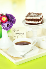 Cup of tea with cakes on wooden tray on table in room