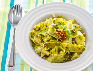 Tagliatelle pasta with pesto and walnuts on white plate